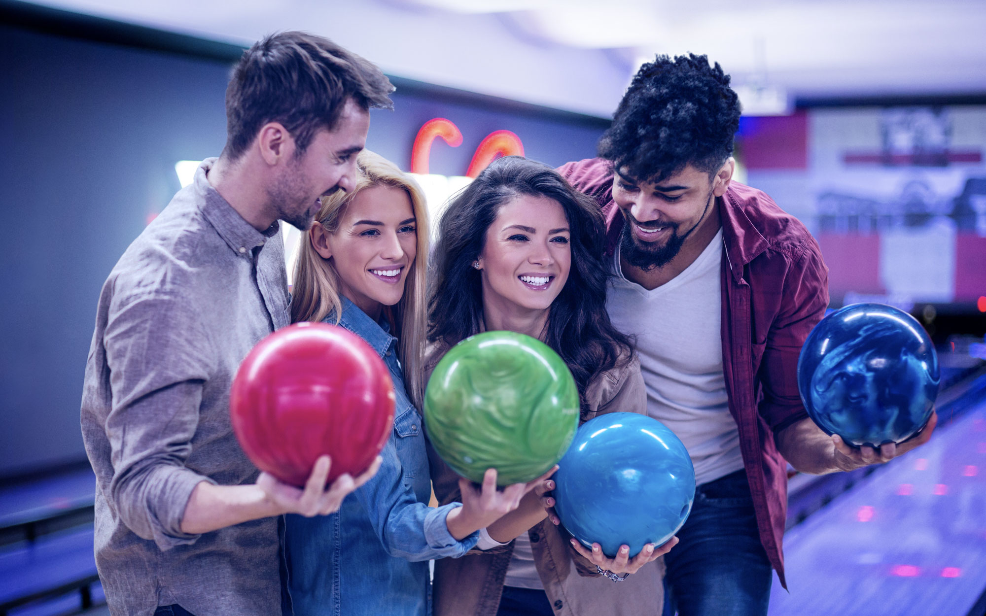 Four smiling friends holding bowling balls at an private event at Aztec Lanes