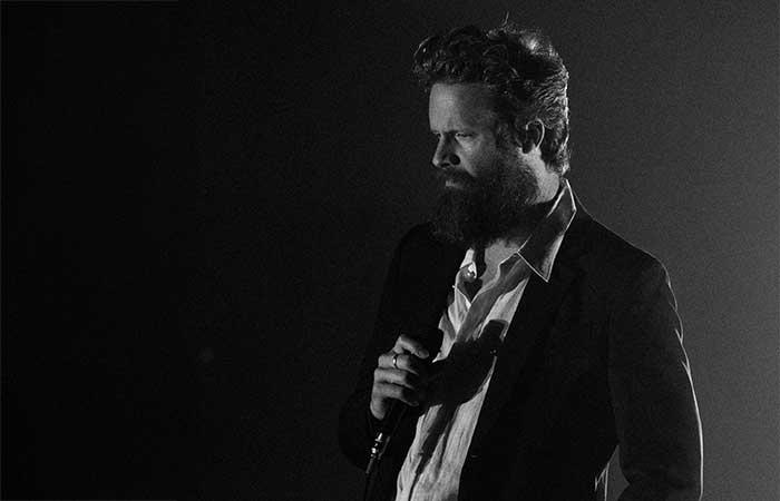 Father John Misty on stage holding a microphone Concert Promo Photo